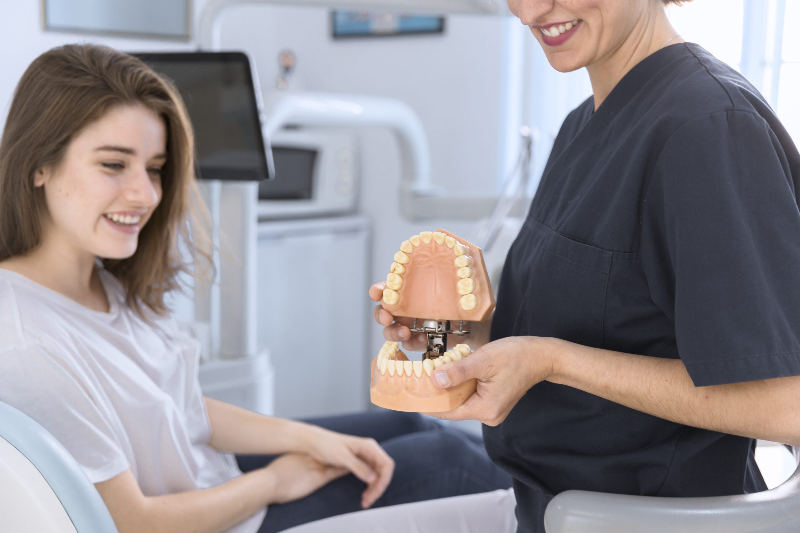 dentium clinica dental - Servicios - primer plano de un dentista que muestra el modelo de los dientes al paciente sonriente scaled